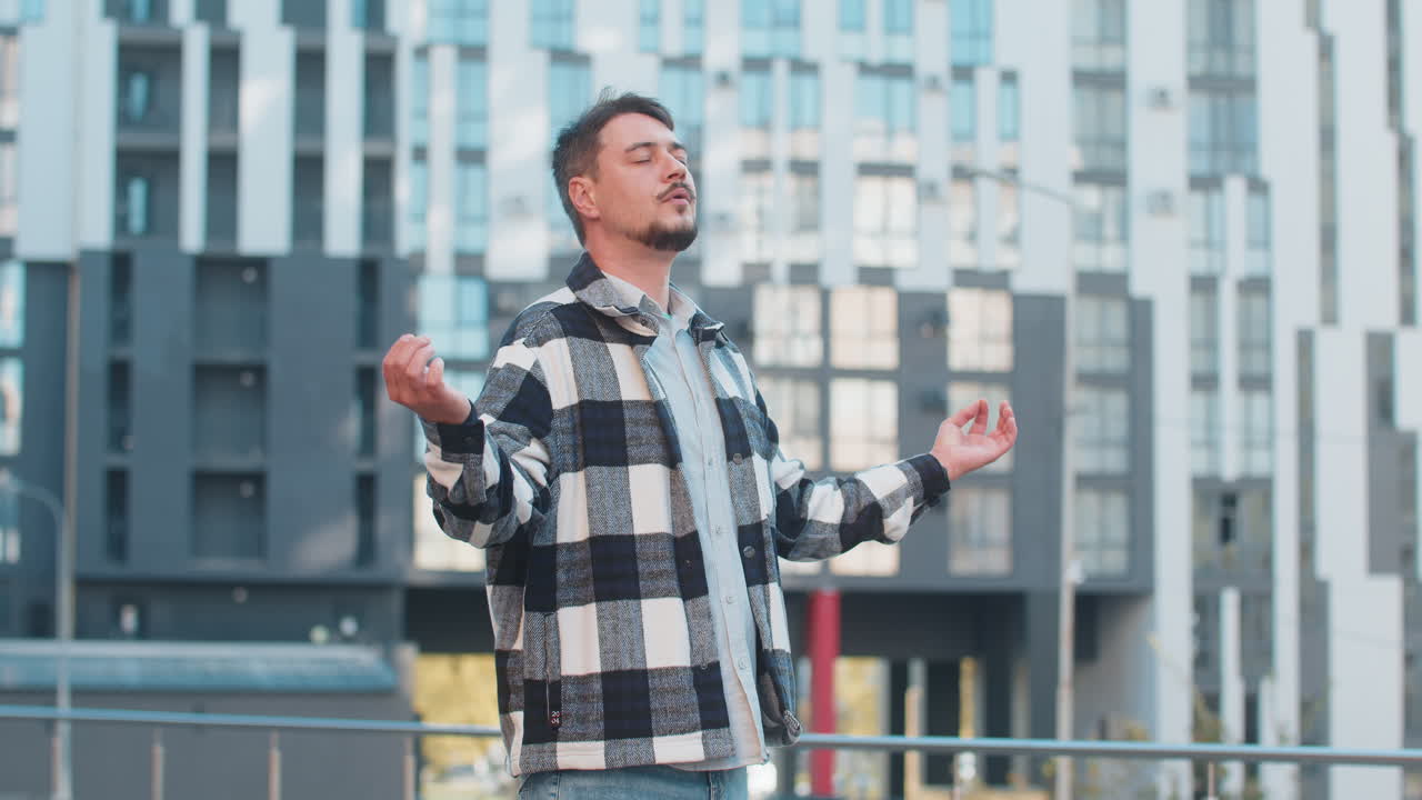 Mature man tourist with arms outstretched meditating with closed eyes standing on downtown street