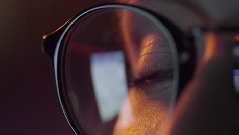 close-up of person wearing glasses, looking at computer screen at night.