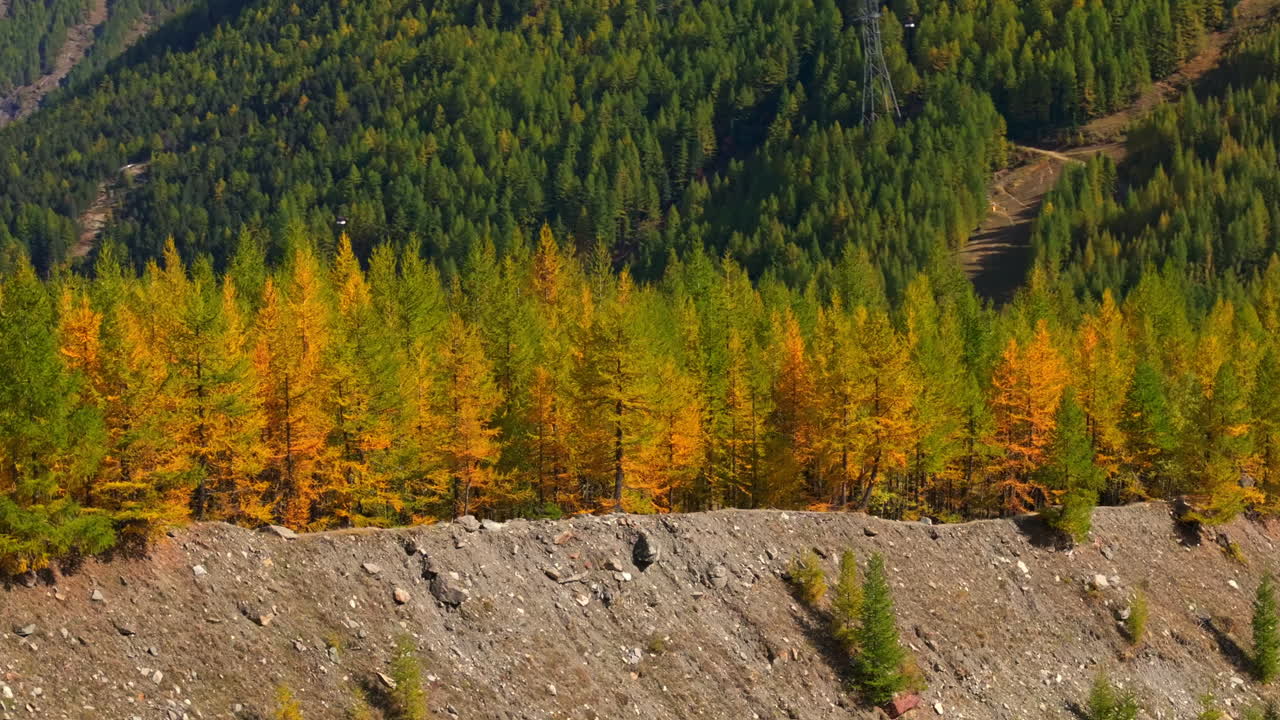 Stunning aerial footage of Saas-Fee in autumn. Golden forests surround the alpine village, nestled in the Swiss Alps. Vibrant fall colors and majestic peaks highlight the beauty of the season.