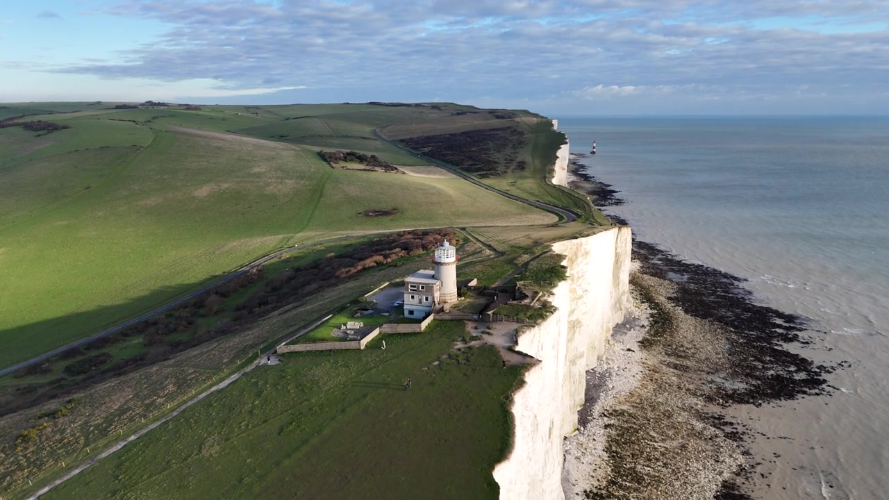 Vue aérienne par drone montrant les falaises des Sept Sœurs avec des falaises de craie blanche, un phare, un sentier côtier et des collines verdoyantes au bord de la mer le long de la côte sud de l'Angleterre