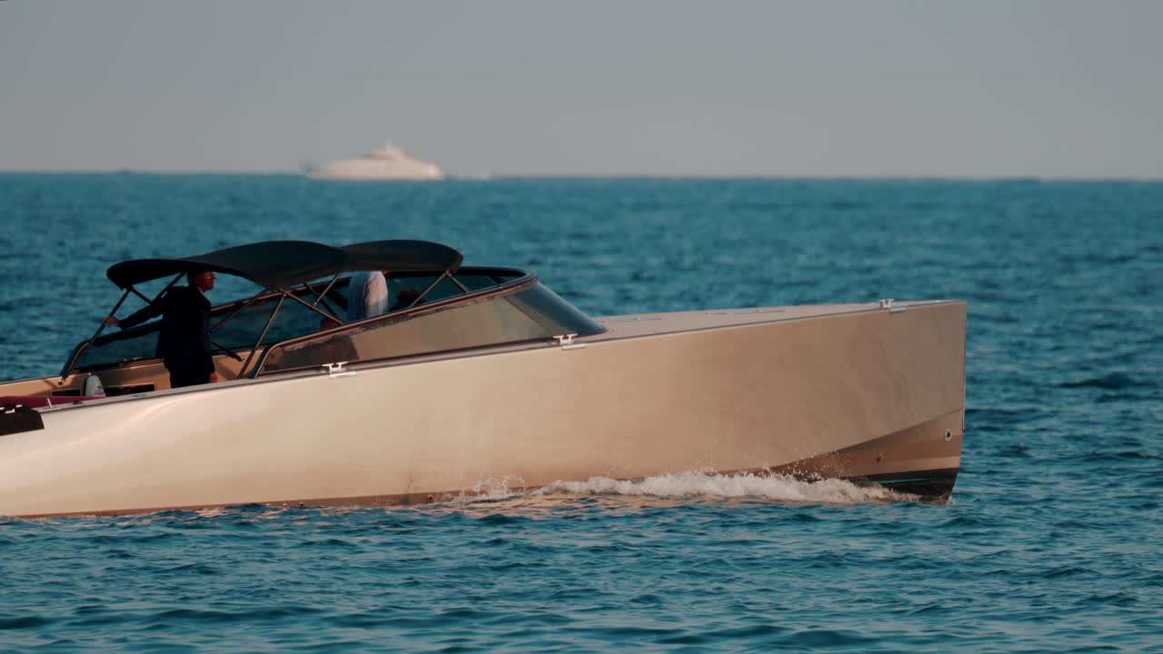 A sleek beige motorboat glides across calm blue waters with sunlight reflecting off its hull