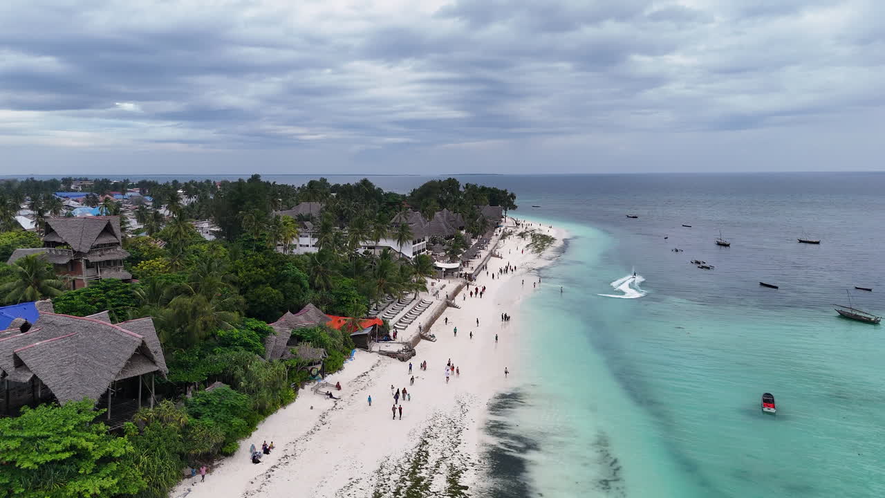 Vista aerea di una vivace spiaggia tropicale con resort e persone, caratterizzata da acque turchesi e sabbia bianca