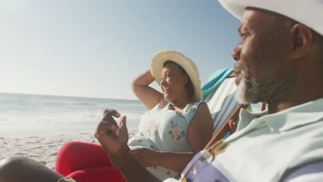 Lächelndes-älteres-Afroamerikanisches-Paar,-Das-Auf-Sonnenliegen-Am-Sonnigen-Strand-Liegt