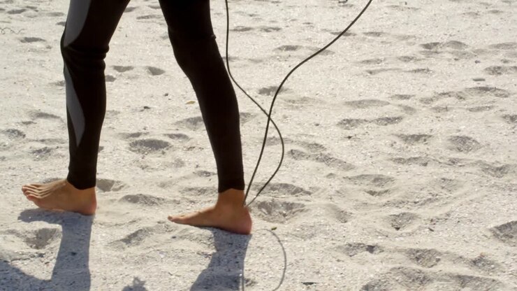 Donna che cammina con tavola da surf sulla spiaggia 4k