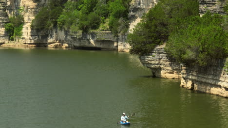 un kayakista remando cerca de escarpados acantilados de piedra caliza a lo largo de un tranquilo lago bordeado de árboles