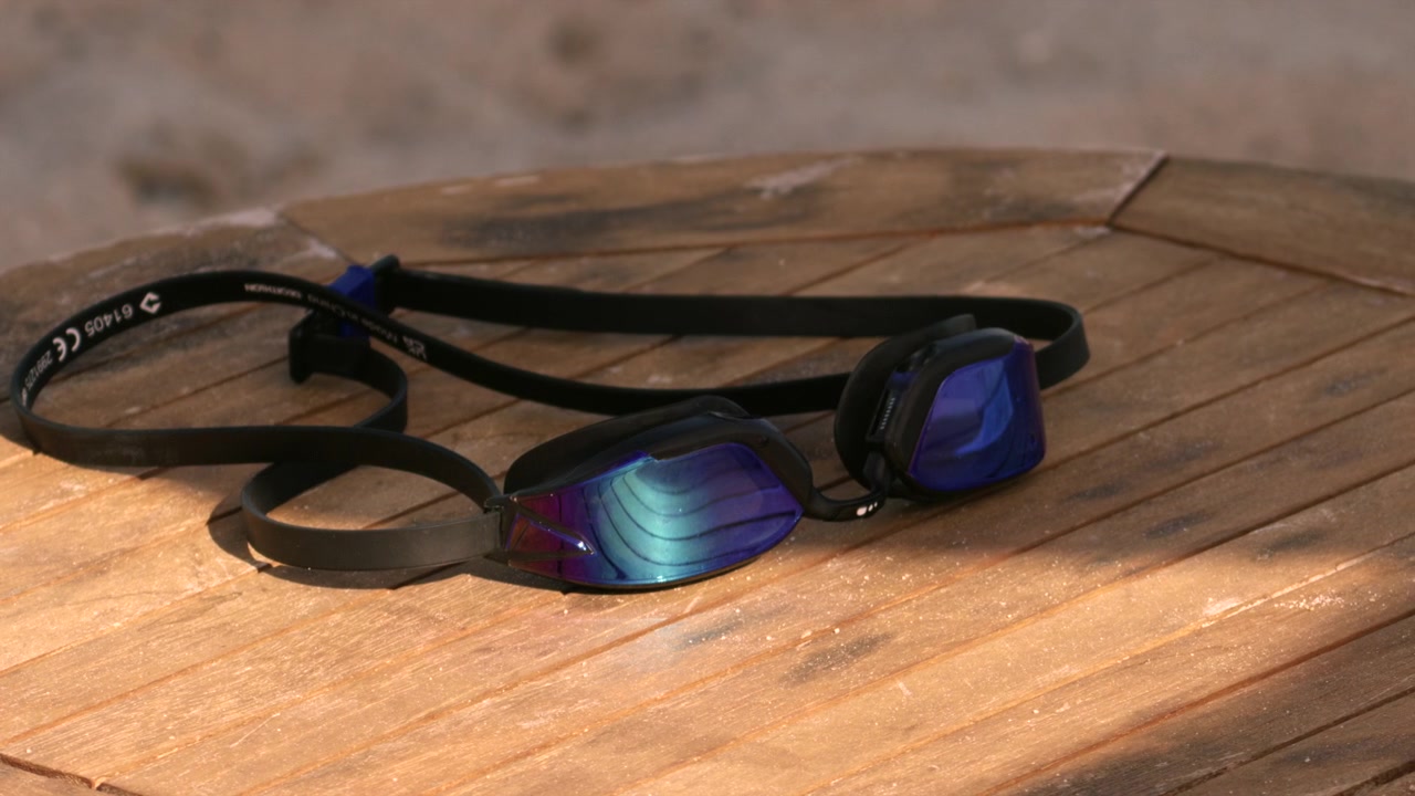 Swimming goggles with mirrored lenses sitting on a wooden table outdoors, ready for a swim or training session