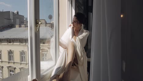 bride in boudoir dress sitting on window sill wedding morning preparations woman in night gown, veil