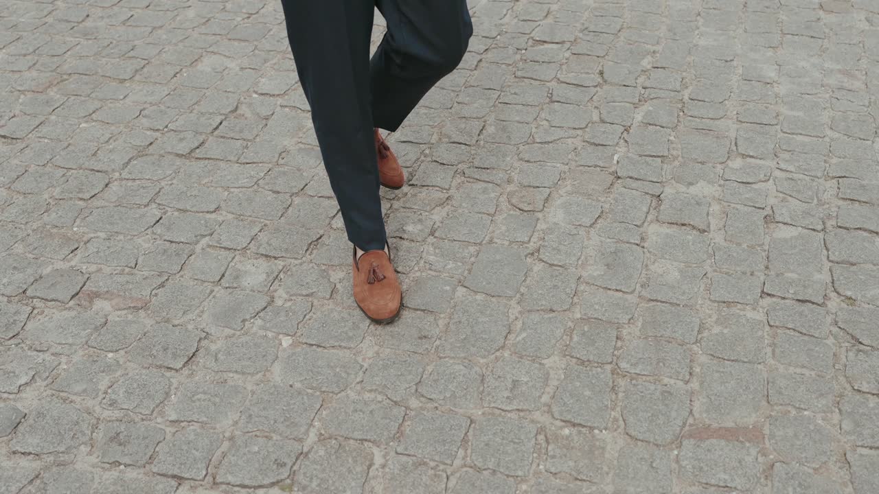 close up of groom walking on cobblestone street wearing elegant brown tassel loafers
