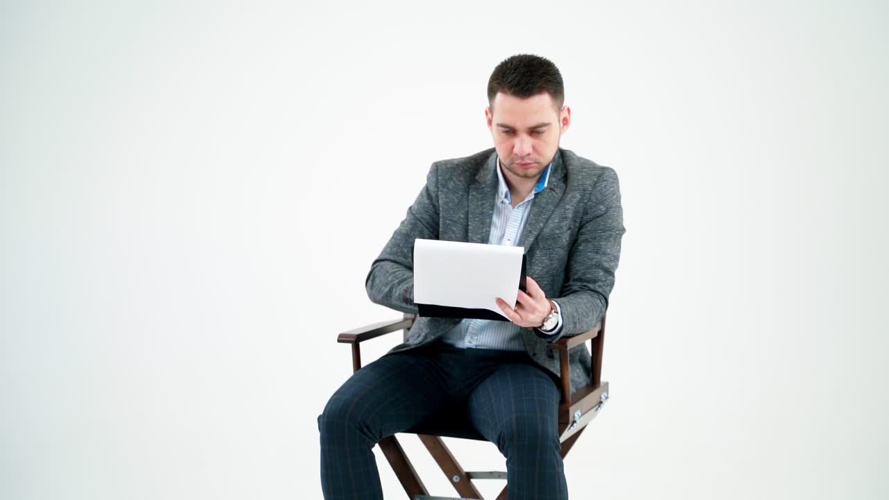 Handsome businessman reading documents. Young man in grey suit sitting on a wooden chair and looking the paperworks on white background.
