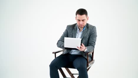 handsome businessman reading documents. young man in grey suit sitting on a wooden chair and looking the paperworks on white background.