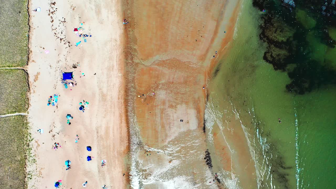 Aerial bird’s-eye drone flying straight down on Saco, Maine beaches filled with people. Vacationers walk the sand near houses as the Atlantic Ocean waves roll along this beautiful East Coast shoreline