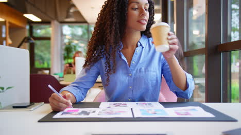 businesswoman sitting at desk in open plan office approving or checking proofs or design layouts