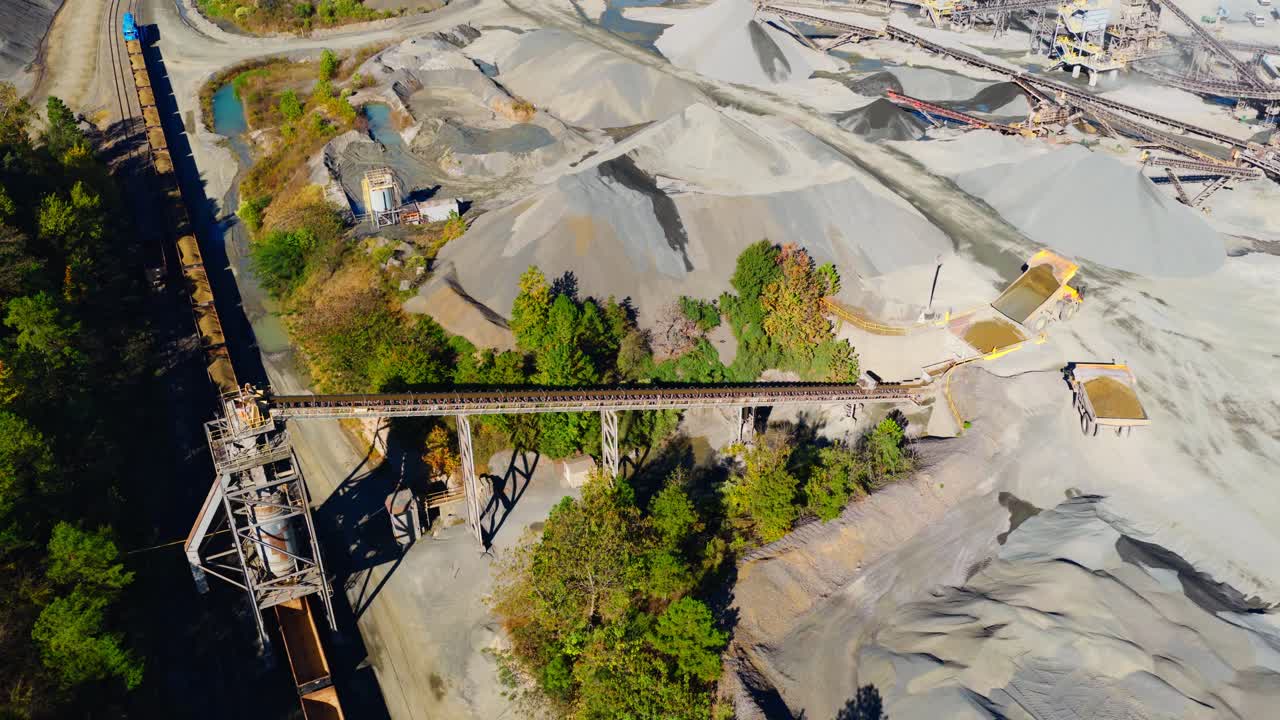 Drone pullback reveal of quarry with freight train loading containers and aggregate piles, complex industrial backdrop
