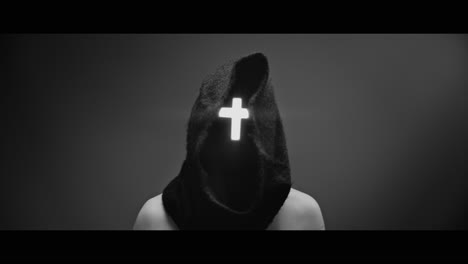 masked and hooded man with cross of light glowing on his face rise his head