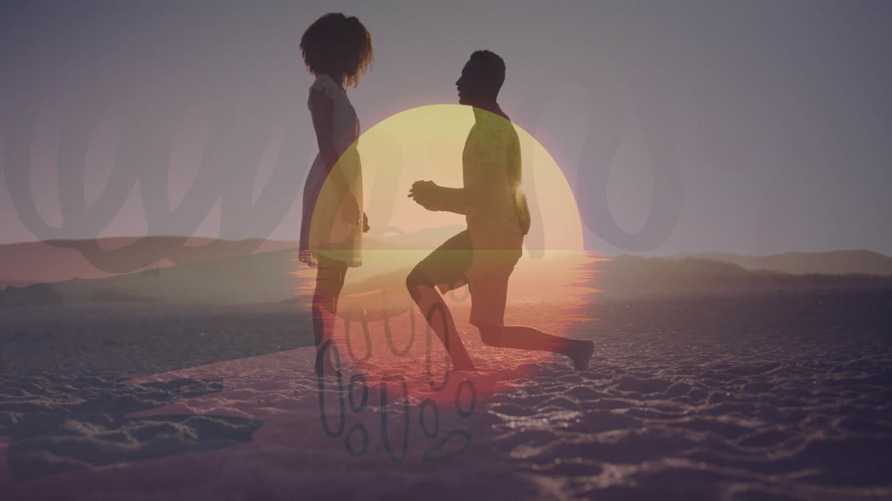 Silhouetted couple walking on sandy beach with sunset in background