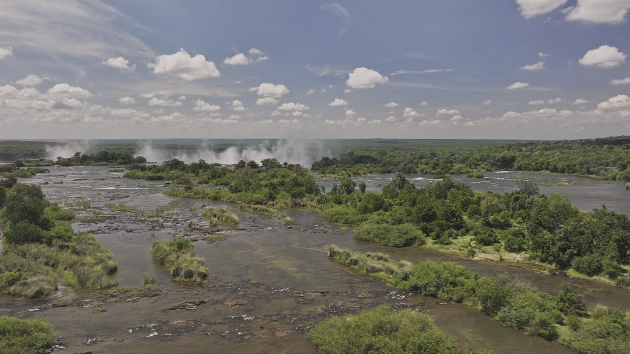 Victoria Falls Zimbabwe Aerial v1 low flyover Zambezi River, following the water flow towards the cliff, with a misty curtain amidst lush green landscapes - Shot with Mavic 3 Pro Cine - Jan 3rd 2024