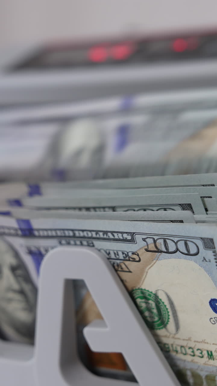 A wad of one hundred dollar bills being counted in cash machine. Apparatus for counting money blurred close up. Vertical video