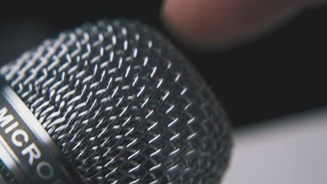 man-taps-on-shining-microphone-by-finger-on-dark-background