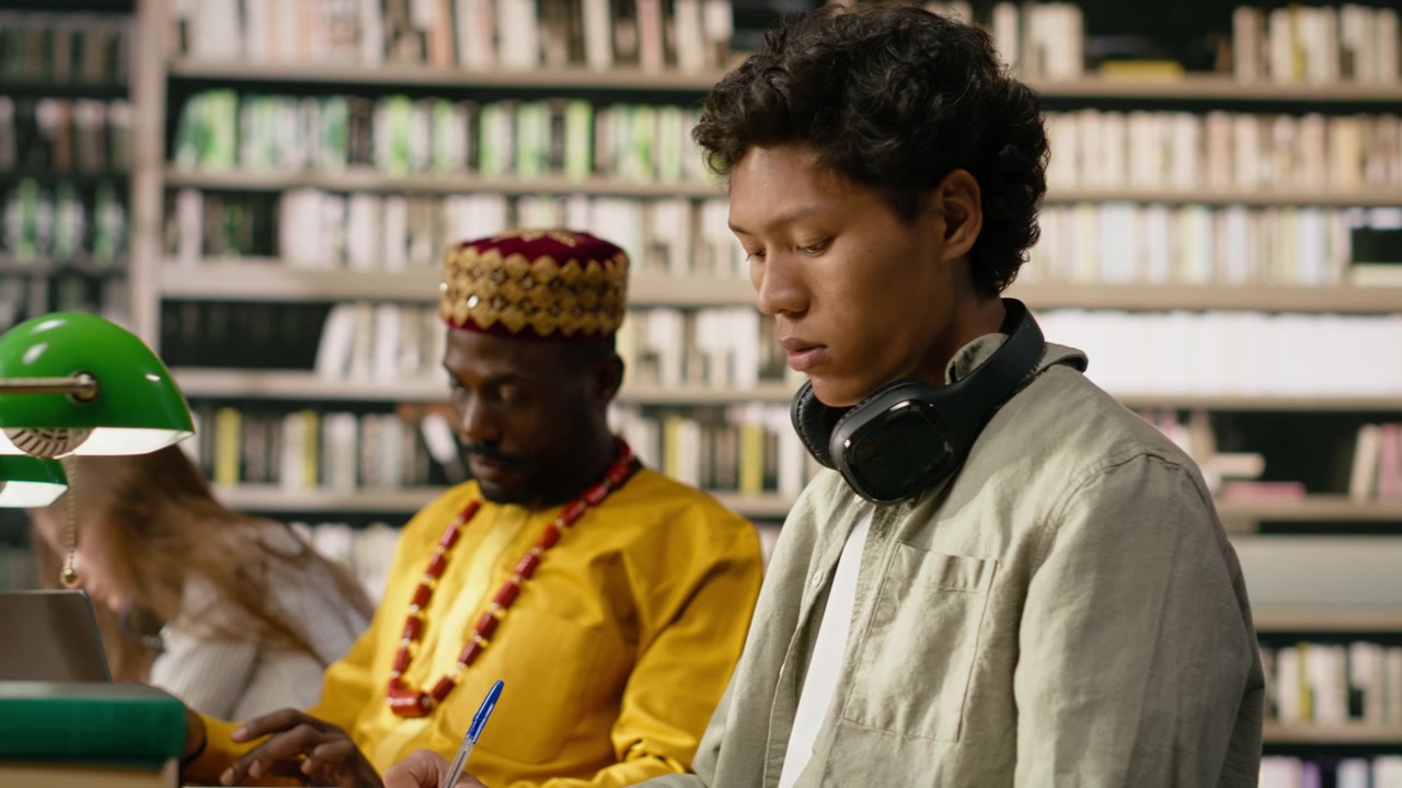 Man student with headphones reads open book in library study area