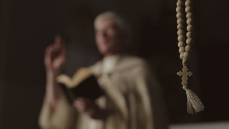 rosary beads and unrecognizable clergyman preaching on background