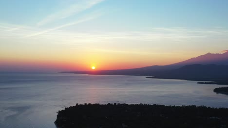 beautiful sunset with colorful sky, yellow sun on bright heaven reflecting over calm clear sea surface around silhouette of tropical island, indonesia