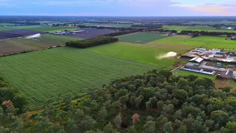 vast fields under dusk clouds. vast agricultural landscape featuring fields, trees, and farm buildings at twilight
