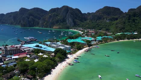 Turquoise-water-laps-gently-at-the-shore-of-a-tropical-island,-with-boats-dotting-the-seascape-and-lush-green-hills