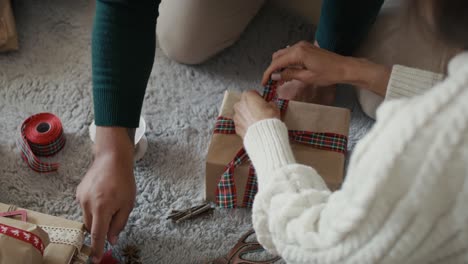 High-angle-view-of-hands-of-unrecognizable-couple-packing-Christmas-present-together-at-home.