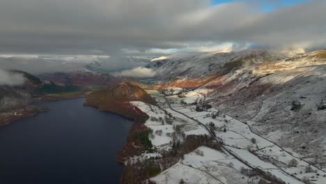 Dark-lake-and-valley-road-with-mountains-covered-in-cloud-and-light-snow