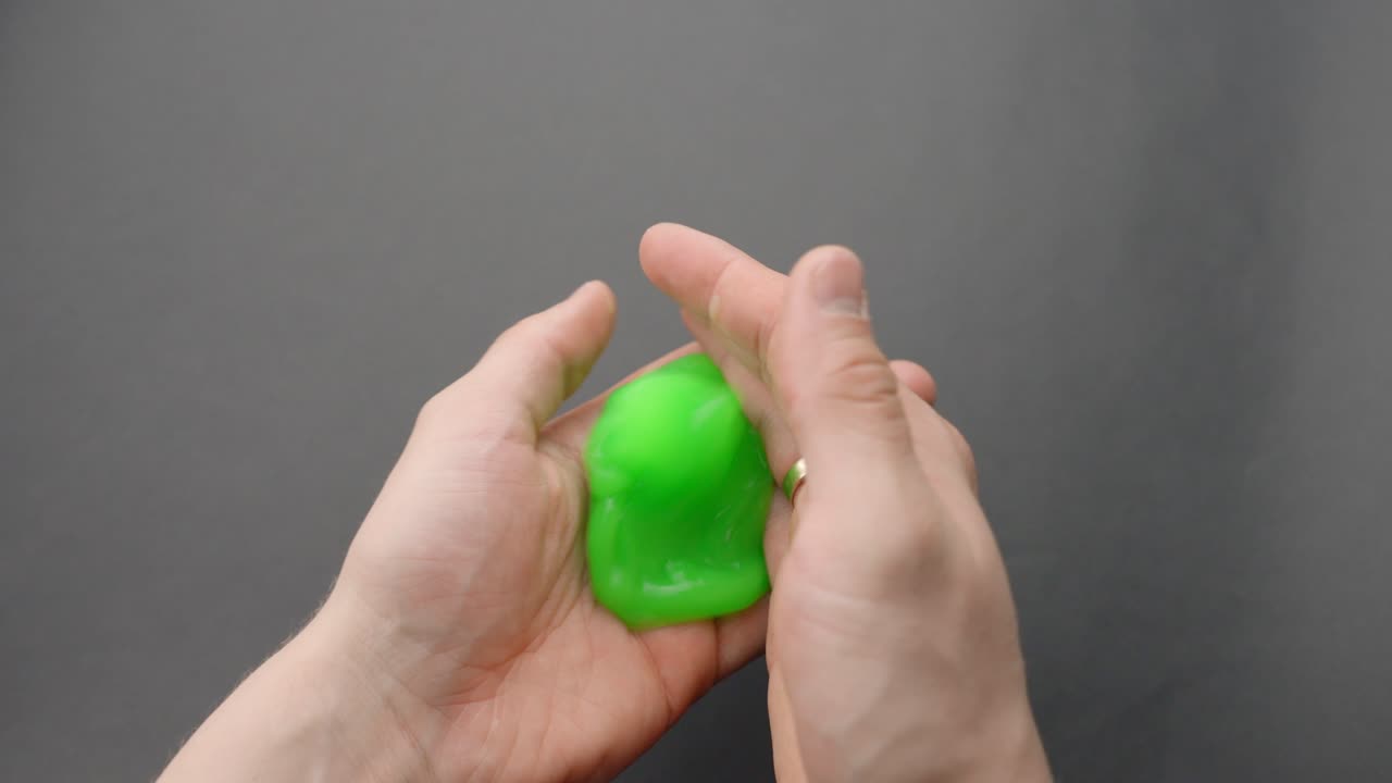 Hands playing with bright green slime ball on grey background, pov