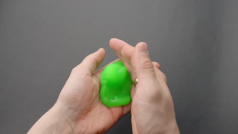 hands playing with bright green slime ball on grey background, pov