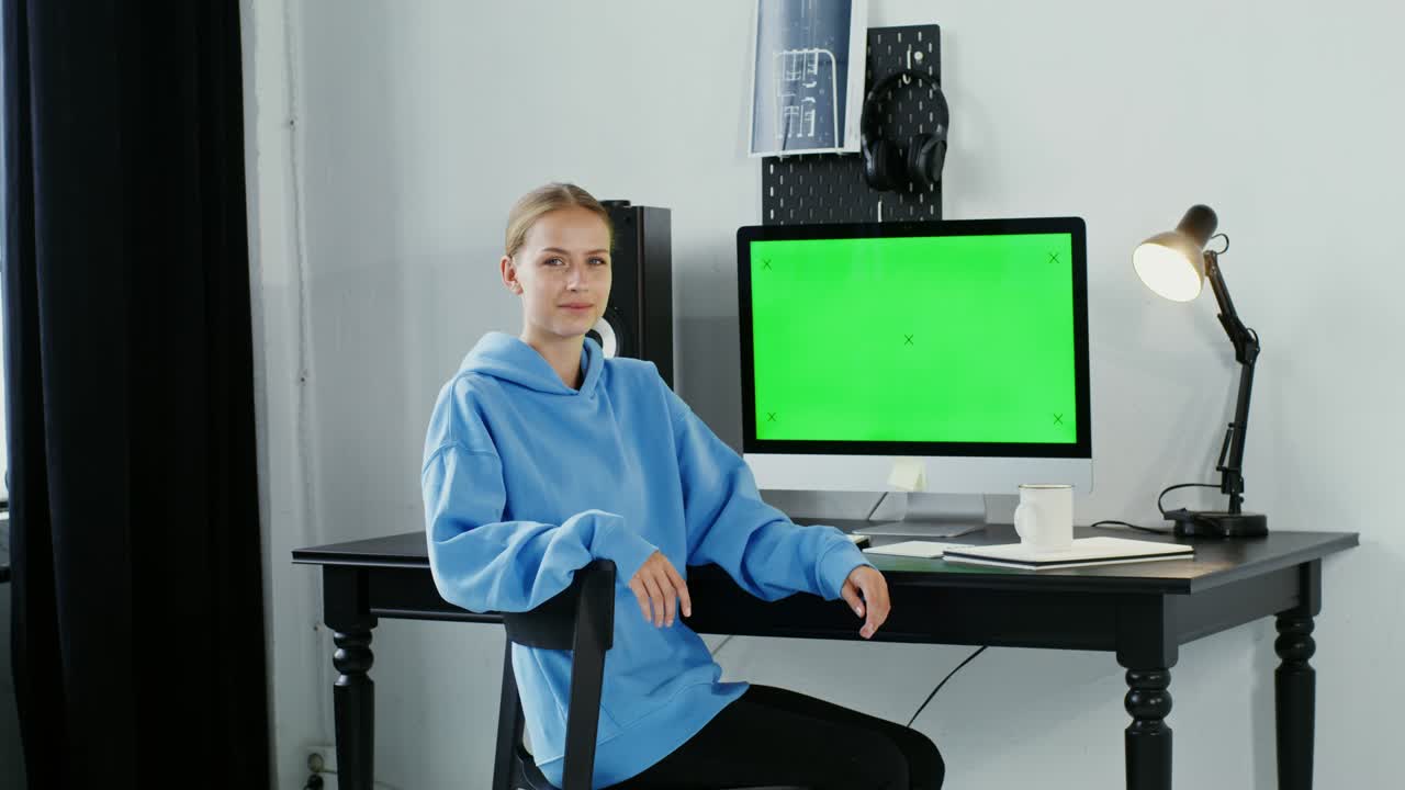 Young woman smiling looking at the camera sitting in front of a green monitor