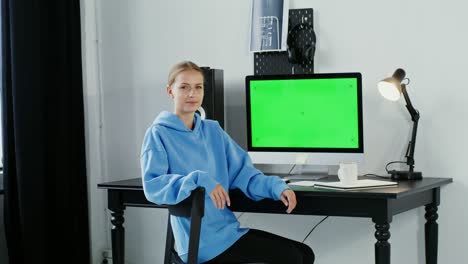 joven sonriendo mirando a la cámara sentada frente a un monitor verde