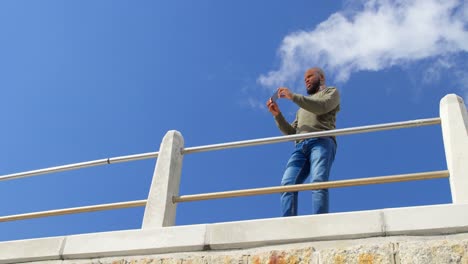 Low-Angle-Ansicht-Eines-Mannes,-Der-Ein-Foto-Mit-Einem-Mobiltelefon-In-Der-Nähe-Eines-Geländers-Macht,-4K