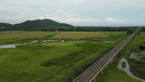 angled aerial footage towards the horizon with hills trees, farmland, and the elevated railway, muak klek, saraburi, thailand