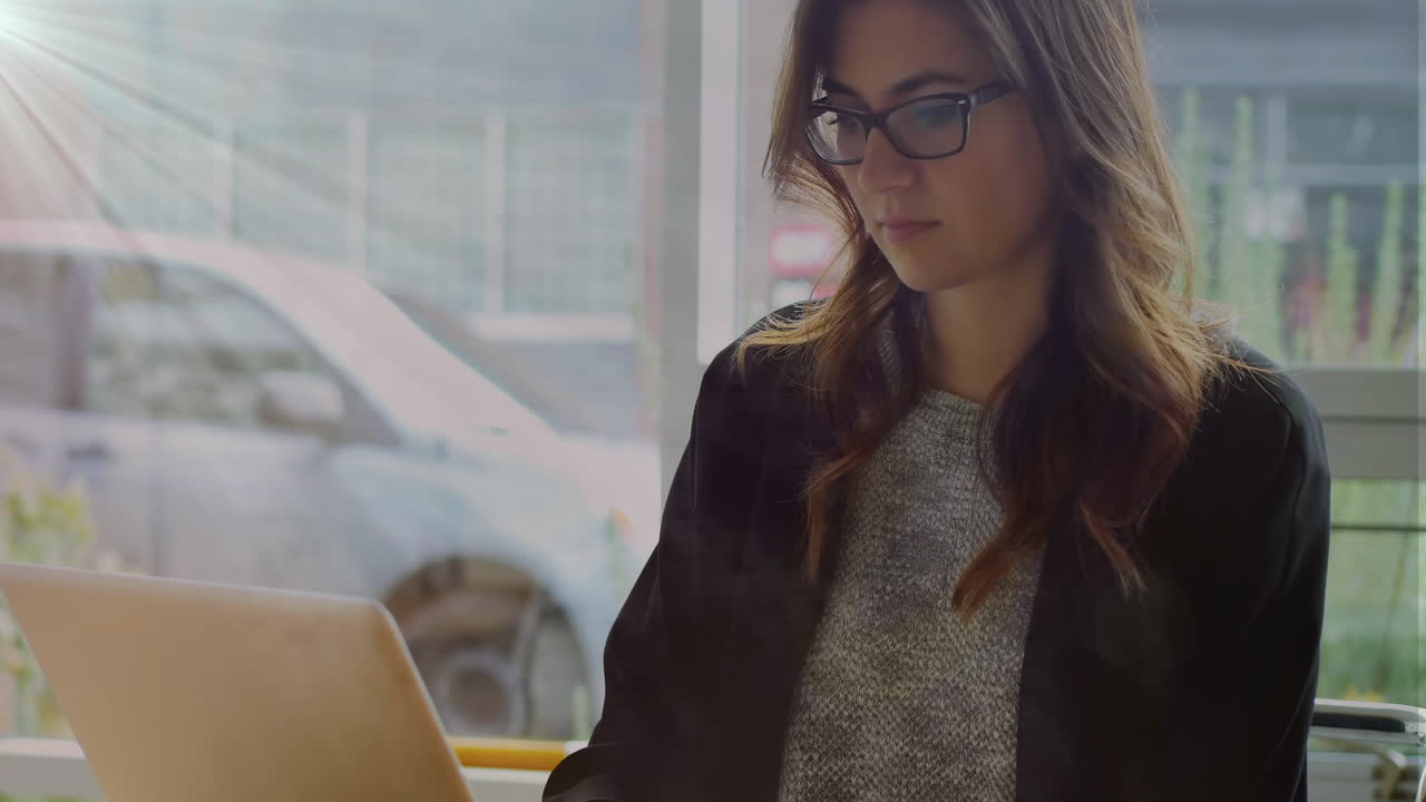 Animación de red de iconos digitales con una empresaria mestiza usando un portátil en una cafetería