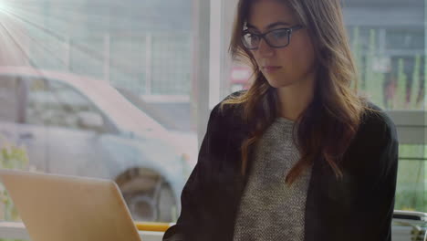 animación de una red de iconos digitales contra una mujer de negocios biracial que usa una computadora portátil en un café