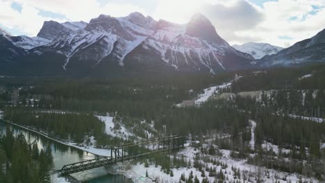 Canmore-Engine-Bridge-with-Rocky-mountains,-Aerial-backwards-ascent,-Canmore,-Alberta,-Canada