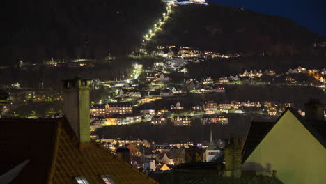 beautiful view of fløybanen funicular in bergen at night, with people wearing headlamps walking up and down the curved roads to the summit