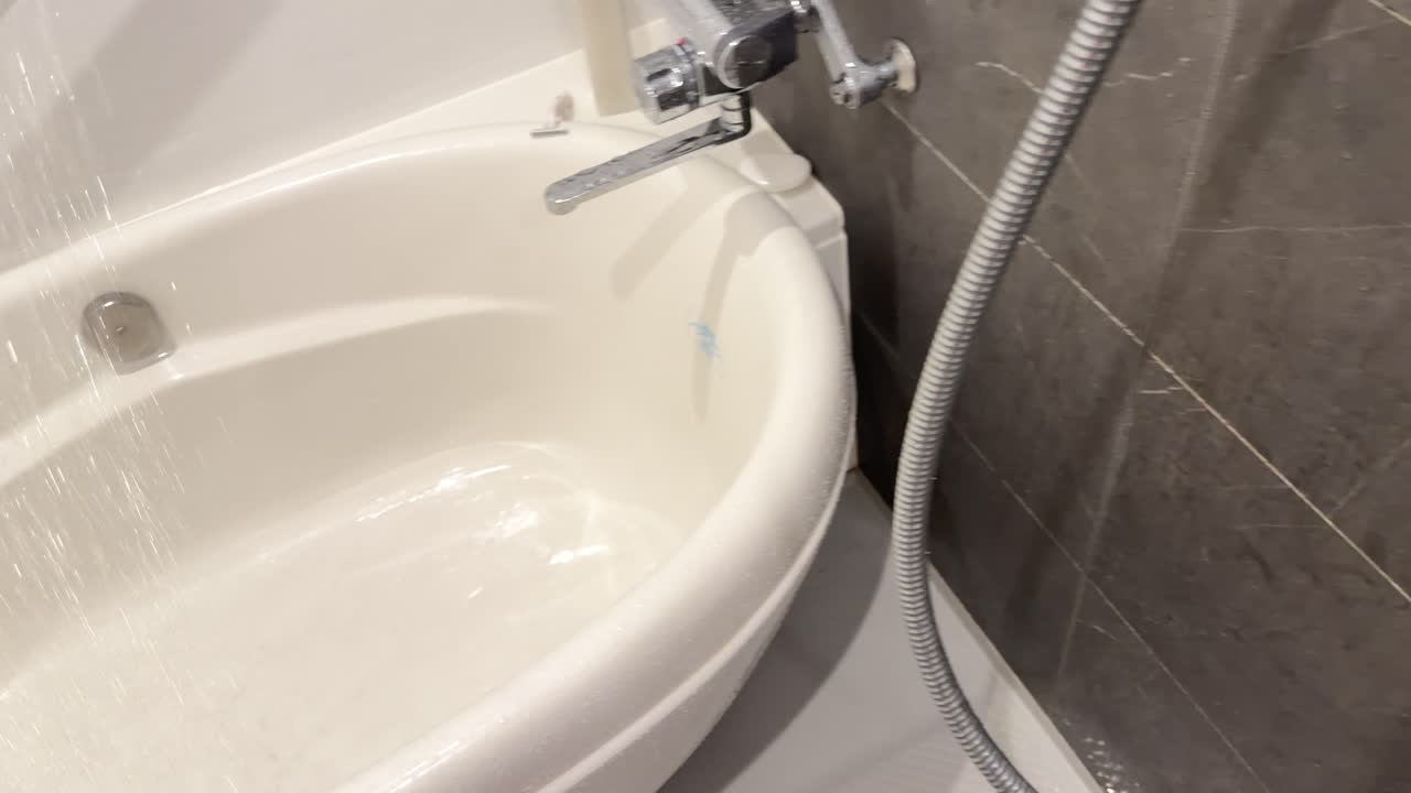 A person turns a chrome handle, activating a shower head to fill a white bathtub