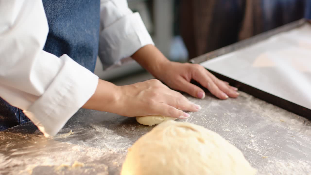 African American woman in apron cutting proofed dough shaping buns for baking at floured table