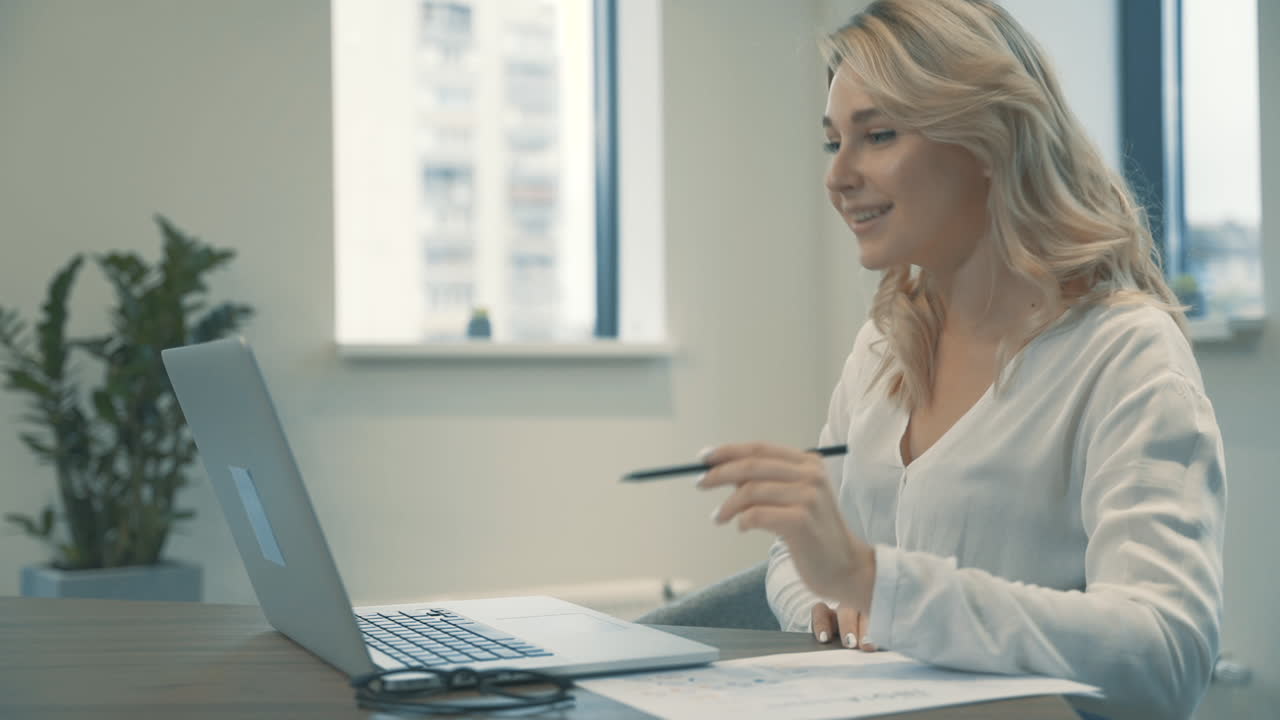 Pretty Young Blonde Woman Having A Business Video Call And Showing Documents With Charts And Graphs