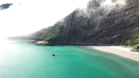 Drone-footage-of-a-boat-in-clear-blue-waters-at-the-island-of-Vaeroy,-Lofoten-Islands-in-Norway