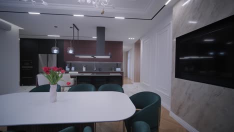 spacious open-plan kitchen with marble island and dining area, featuring modern lighting fixtures, herringbone wood flooring, and teal accent chairs