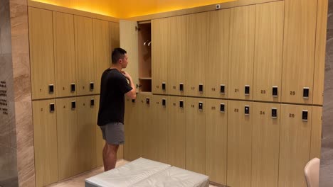 hombre asiático del milenio desnudándose y colgando la camisa en el armario en un lujoso vestuario