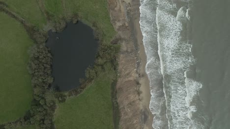 Curracloe-beach-in-stormy-weather,-contrasting-green-fields-and-foamy-waves,-aerial-view