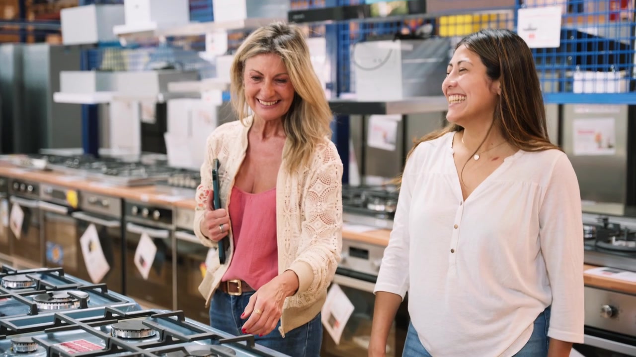 Due donne felici che acquistano un fornello a gas in un negozio di elettrodomestici