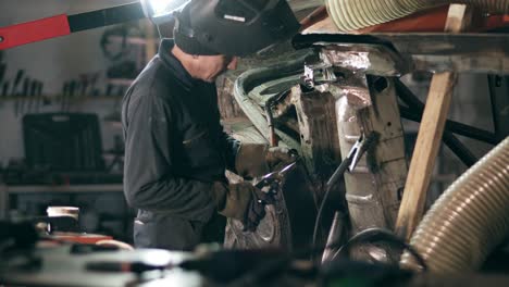 Male-worker-at-a-welding-factory-is-examining-metal-construction-to-weld-some-piece-of-metal-on-it.-Welding-on-an-industrial-plant