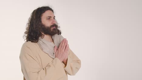 portrait of man wearing robes with long hair and beard representing figure of jesus christ putting hands together in prayer