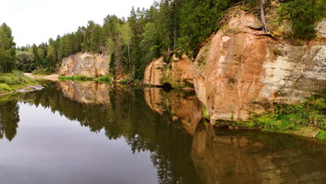 erglu cliffs (eagle cliffs); low aerial drone flyover revealing the largest and most continuous sandstone walls reflecting off the klintis river in gauja national park, latvia.